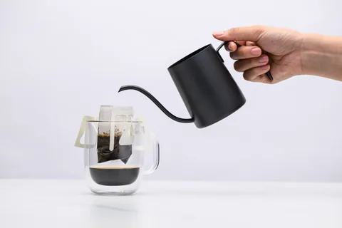 Hot water being poured from a black gooseneck kettle into a Sampan drip bag